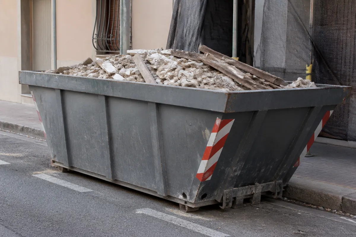Contenedor de escombros lleno junto a la acera frente a una casa en obras en Valencia